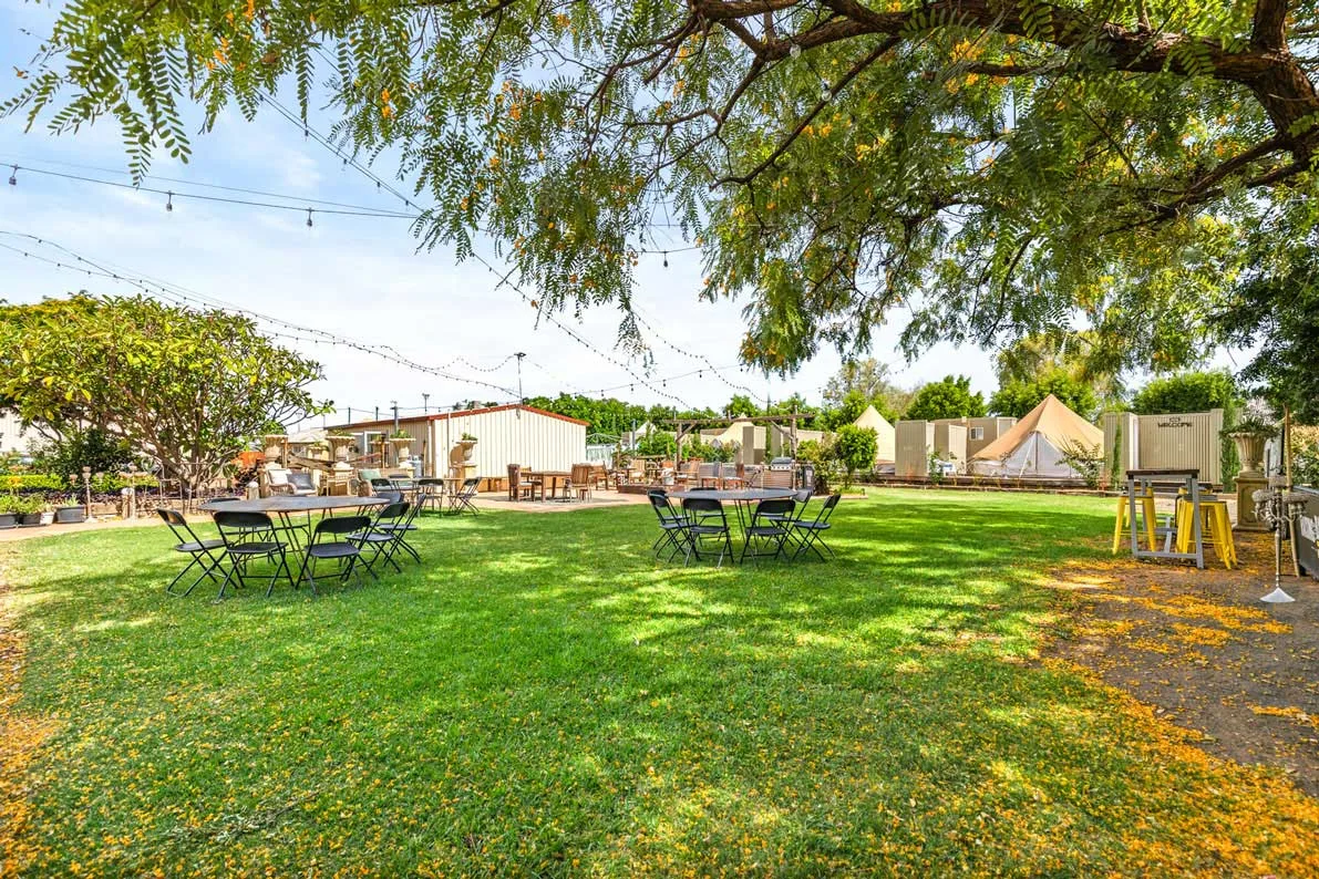 Rear garden lawn at Club Boutique Hotel Cunnamulla with dining tables, festoon lights and glamping tents beneath a wide western sky