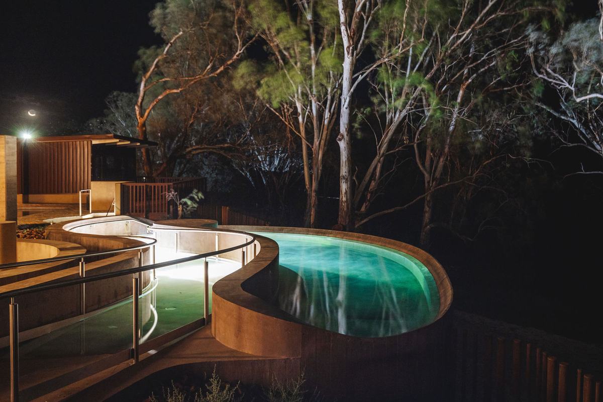 Curved mineral pools at Cunnamulla Hot Springs lit at night beneath floodlit gum trees.