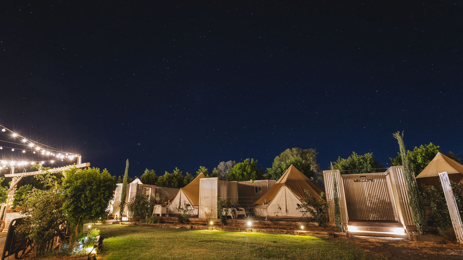 Bell tents and ensuite pods on the hotel lawn lit at night under a star-filled sky.