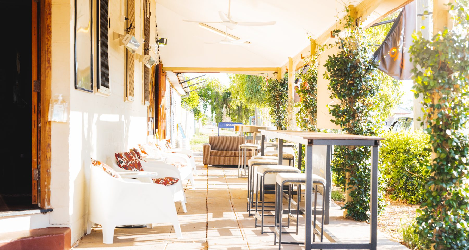 The hotel verandah in the middle of the day: white chairs and high tables in deep shade under ceiling fans, the garden bright beyond.